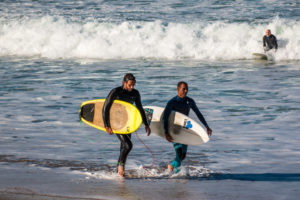 Two surfers walking out of the water with yellow Appletree surfboard end of session